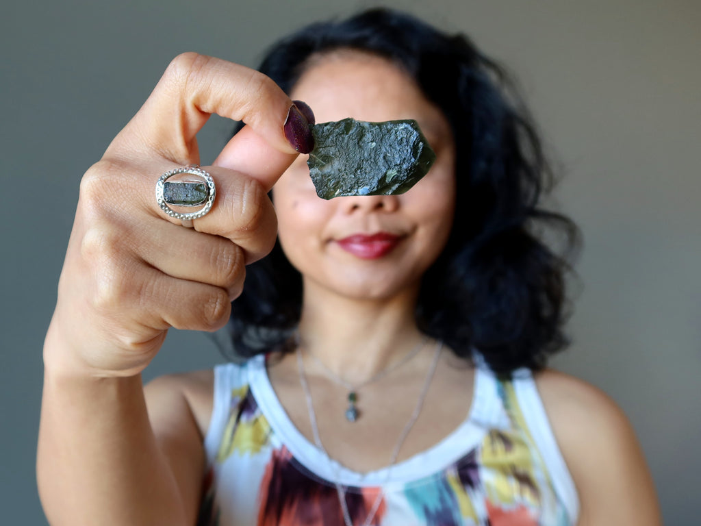 female holding moldavite stone and wearing moldavite ring