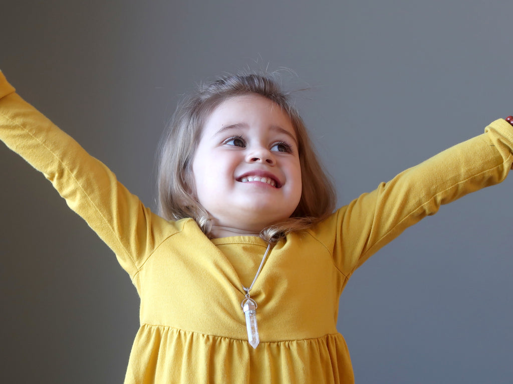happy young girl in a yellow dress with her hands in the air wearing satin crystals jewelry