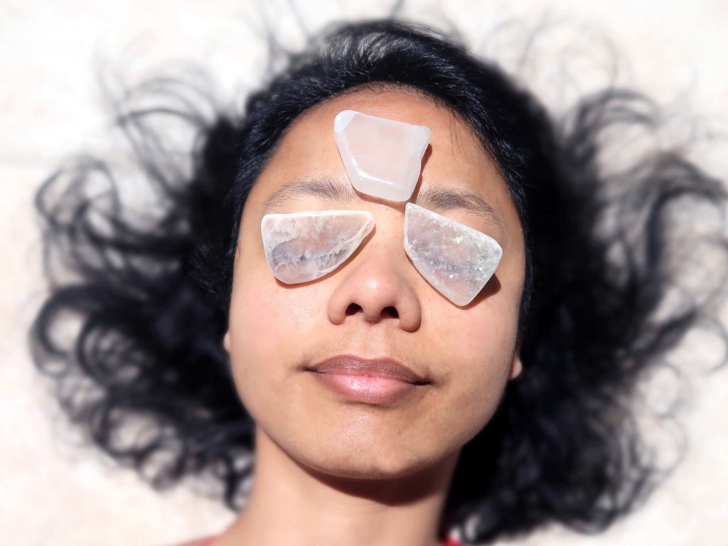 woman lying with ulexite slabs on her eyes and third eye