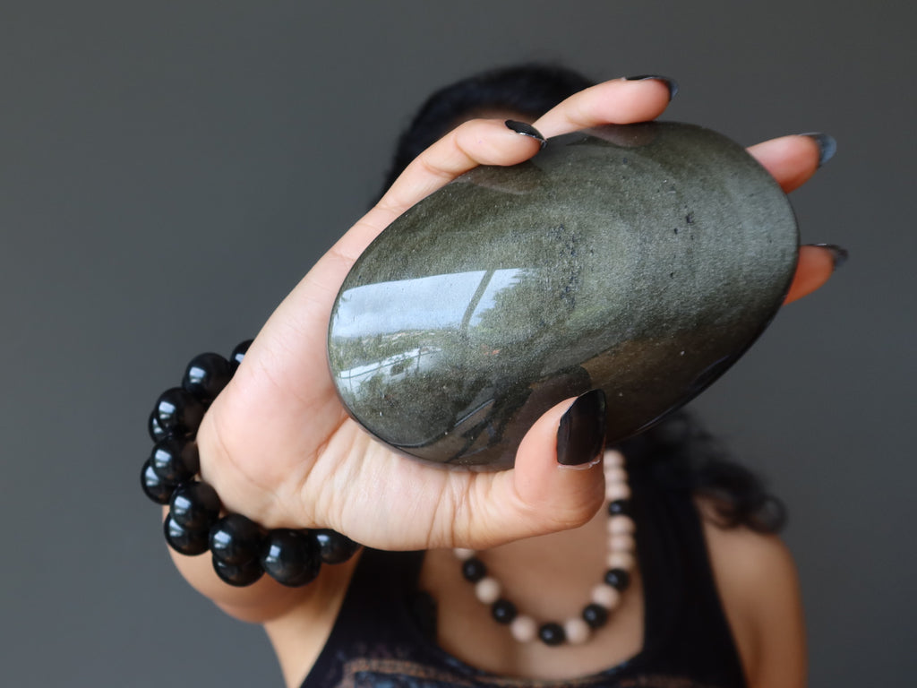 Sheila of Satin Crystals holding out a gold sheen Obsidian palm stone in front of her face