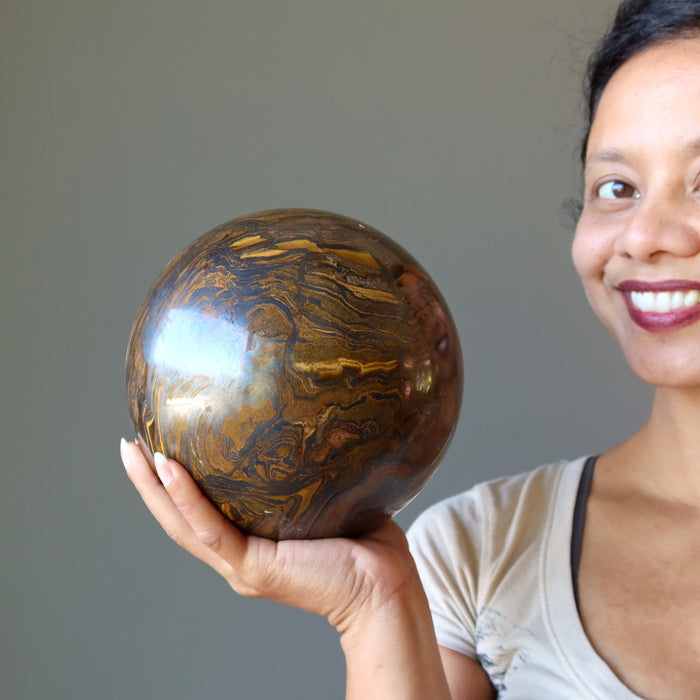 sheila of satin crystals holding a giant brown tiger iron sphere with veins of black hematite