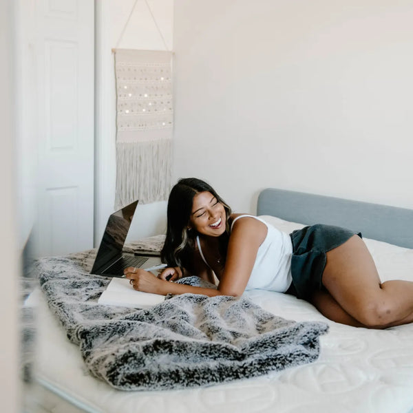 woman laying on bed with laptop and note pad laughing
