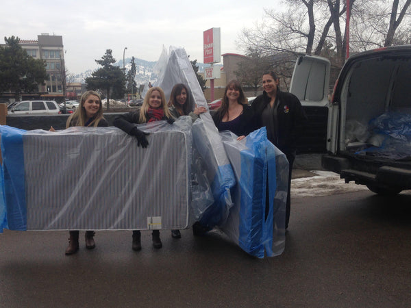 Haven Mattress staff posing with multiple bed-in-box mattresses ready to be loaded into van for donation to those in need