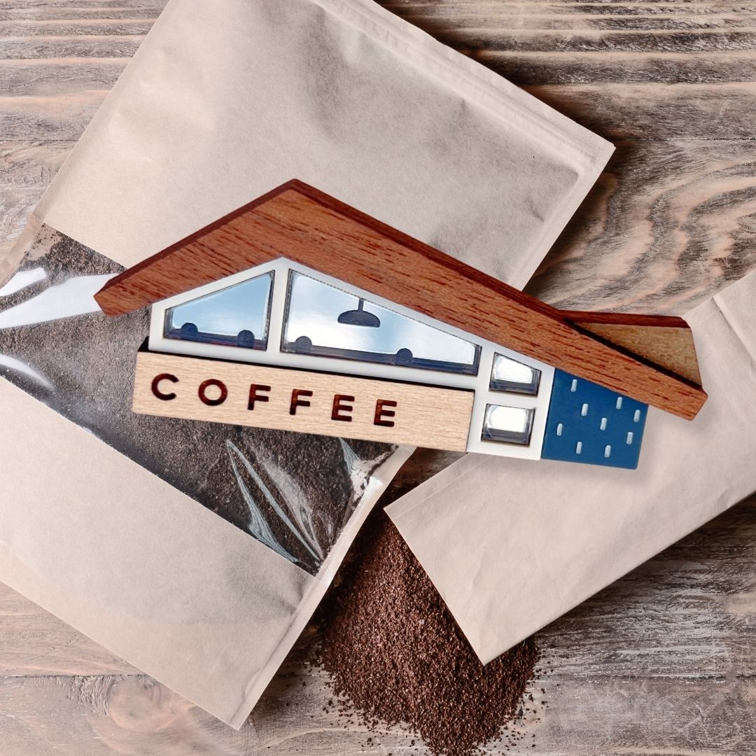 miniature coffee shop brooch with a packet of fresh ground coffee behind