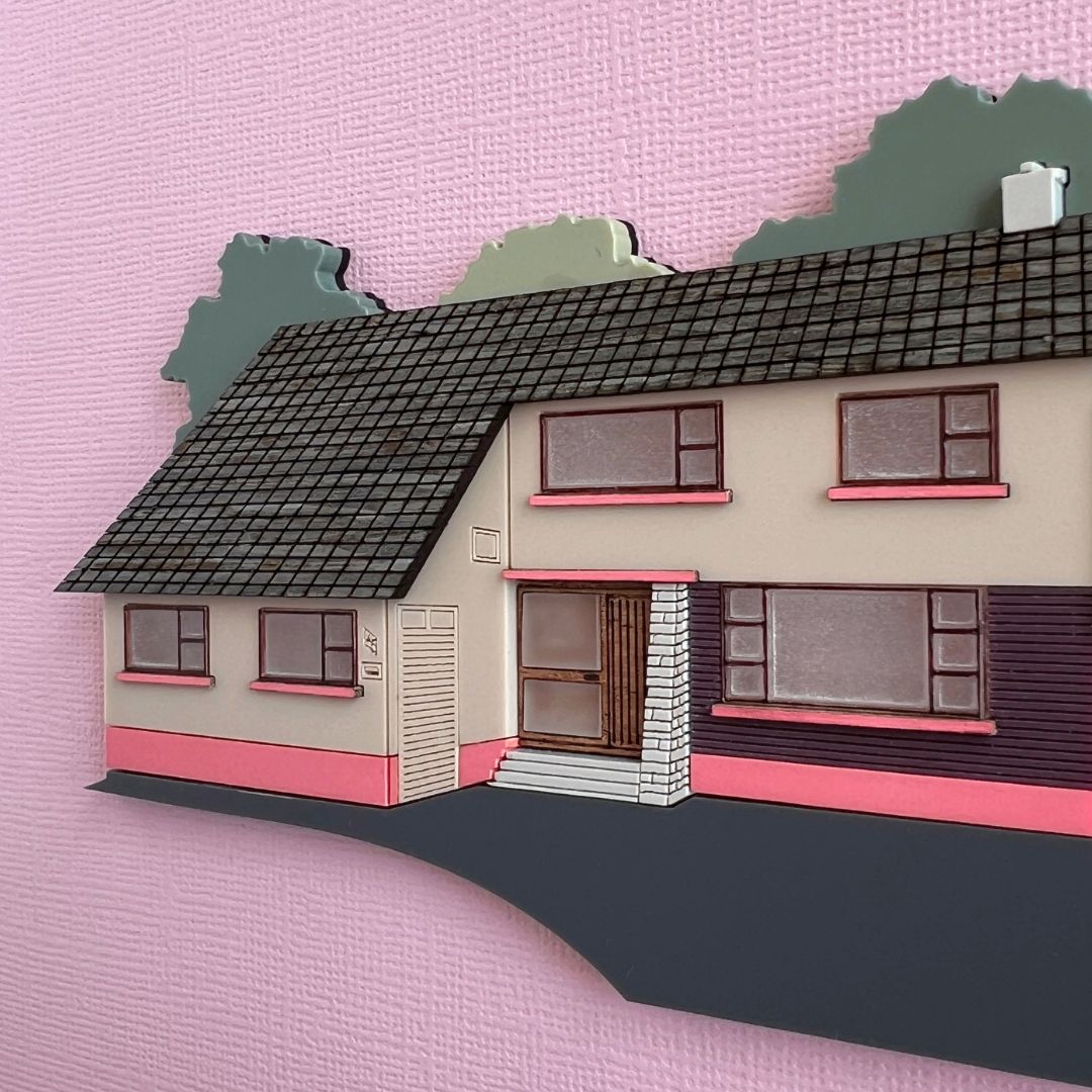 A miniature house artwork made from wood and acrylic on a pink background