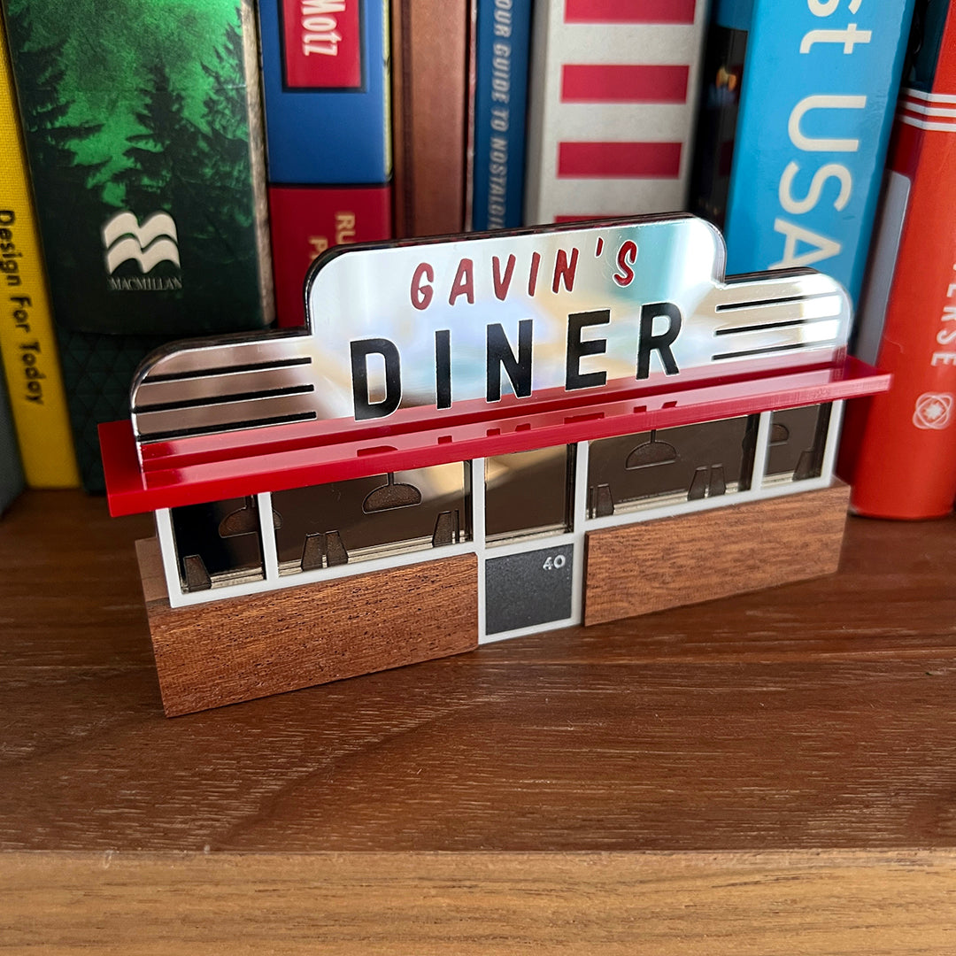 A miniature wooden ornament in the shape of an American diner, photographed in front of a shelf of books