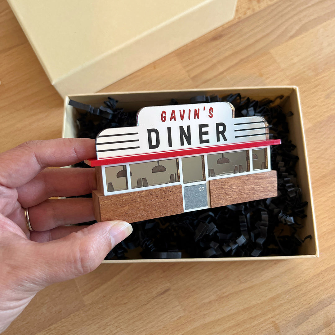 A wood and acrylic ornament in the shape of an American diner, being held in someone's hand