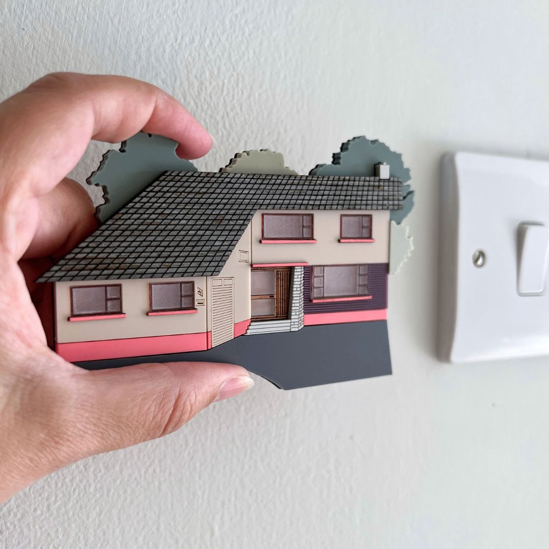 A miniature house facade made from acrylic held in the maker's hand
