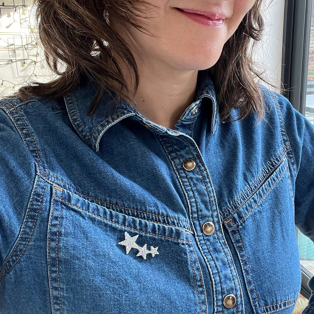 A woman wearing a blue denim shirt and a tiny glittery star pin attached to it