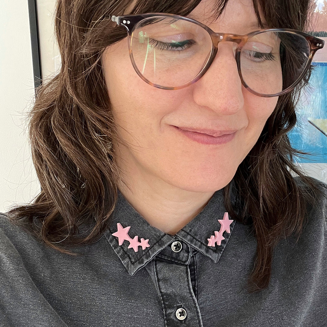 A women wears a denim shirt with pink star shaped pins on the tips of the shirt collars.