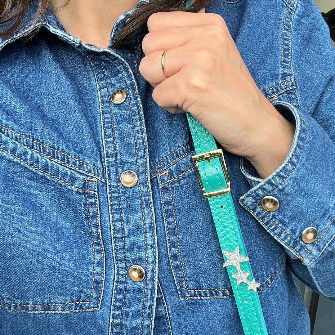 A woman in a blue denim shirt holding a green bag strap with a silver glitter star pin attached to it.
