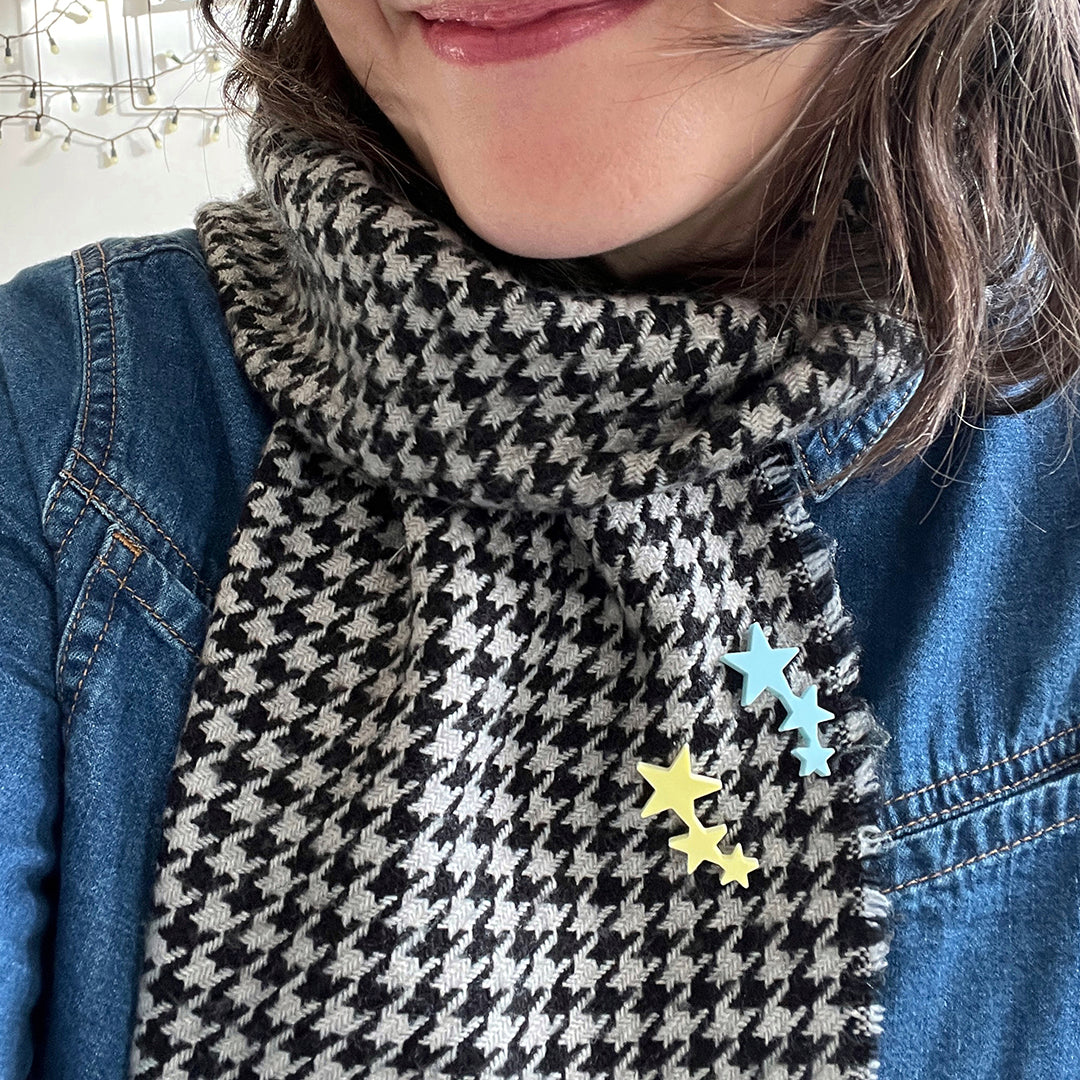 Close in on a woman wearing a houndstooth scarf with two star shaped pins attached to it.
