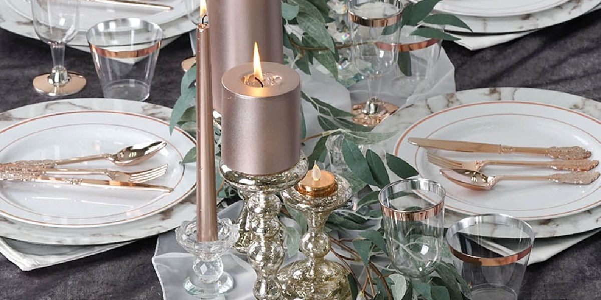 table setting with chargers, golden utensils, and lit candles