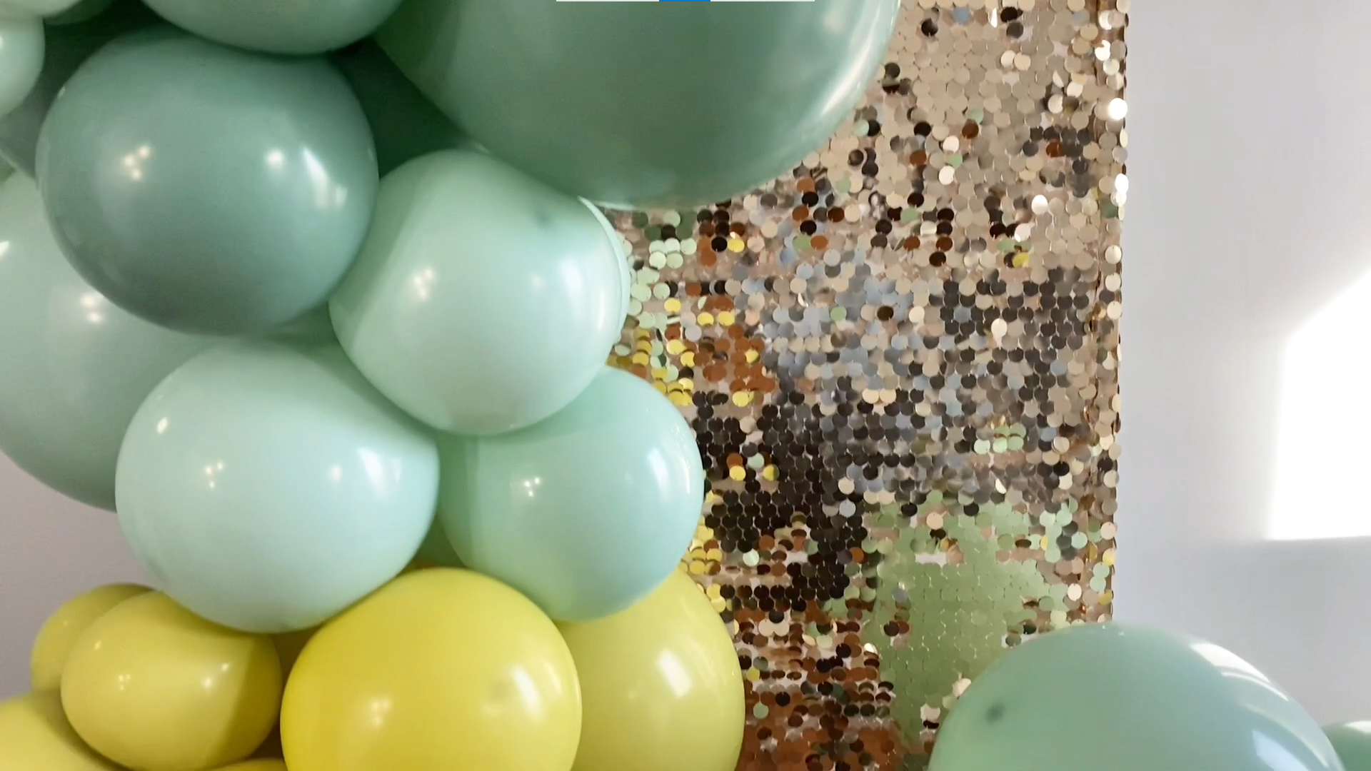 Green and gold balloons against a sequin backdrop