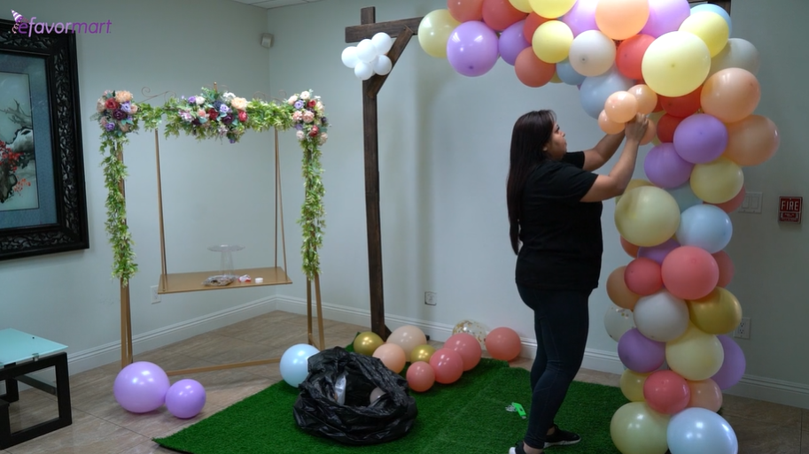 Woman attaching balloon garland to the wooden arch backdrop stand