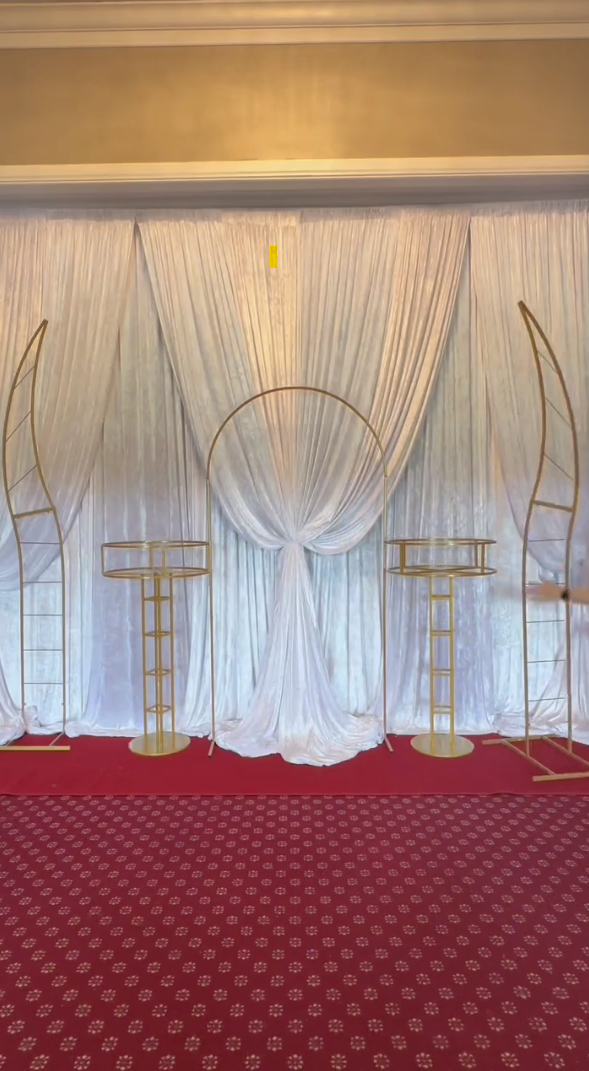 A wedding arch, flower pedestals, and flower stands against a curtain backdrop