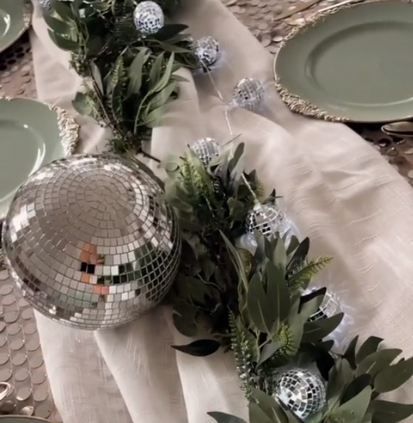Greenery, disco balls, and lit disco ball string lights displayed on the table