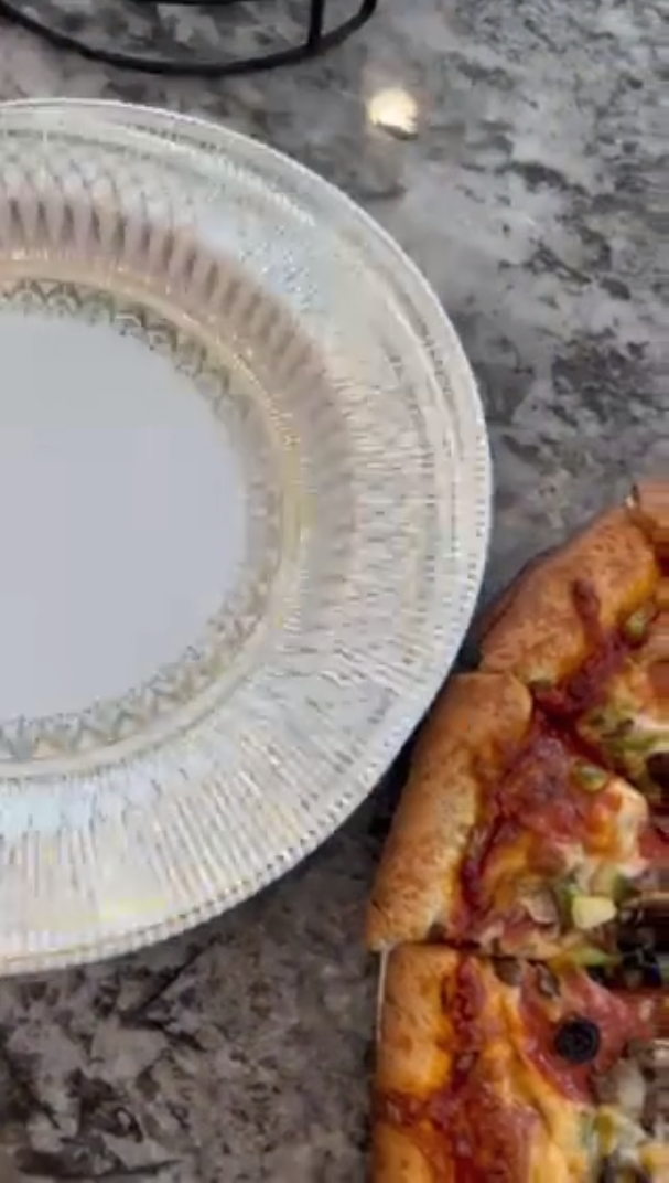 Disposable paper plate beside a pizza