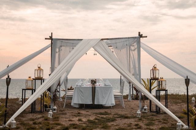 Wedding tablescape by the sea under a sunset-draped canopy.