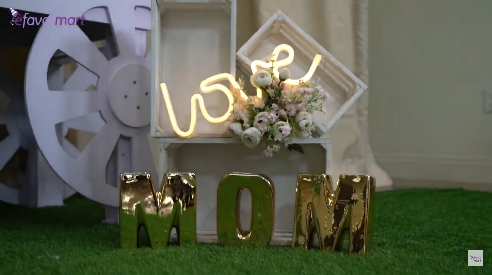 Close-up of a Mother's Day decor setup with glowing 'love' neon sign and floral decorations.