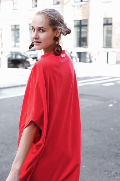 A woman walking on the street wearing red knee-length t-shirt dress with large earrings