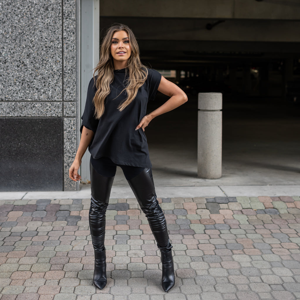 A woman wearing an asymmetrical black t-shirt with a long and short sleeve in organic cotton by Malaika New York