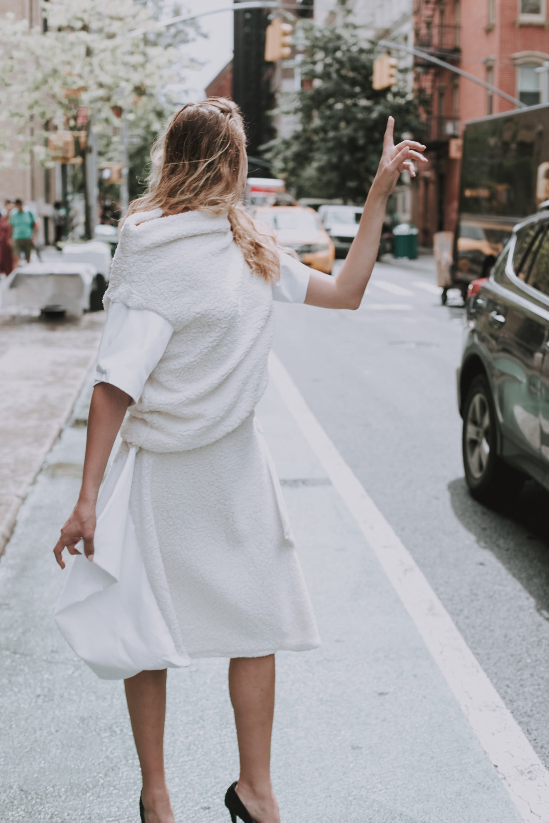 A model standing and getting a cab in Soho Manhattan in her vegan fur look by Malaika New York. A vegan fur skirt and vegan fur top.