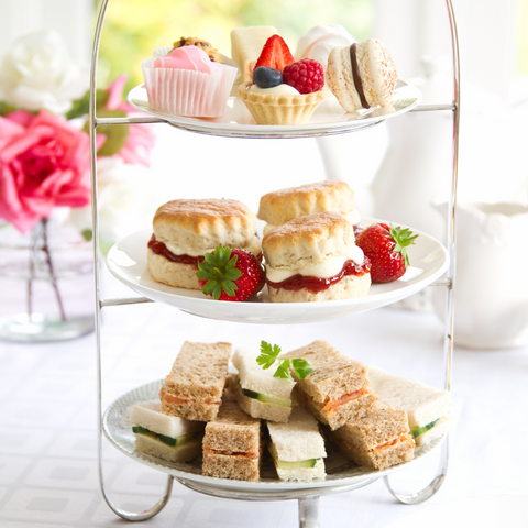 afternoon tea on a raised platter featuring finger sandwiches and scones with cream and jam