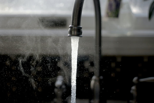 Water running from a kitchen tap with a dark worktop area