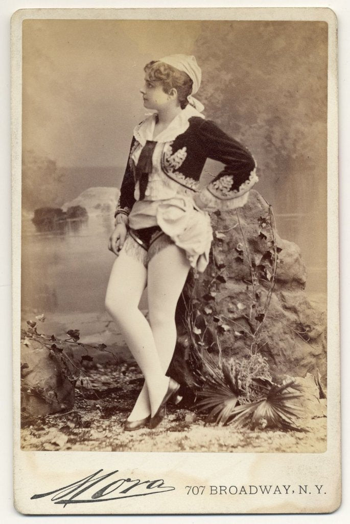 1890. Pauline Hall in short, Greek style costume, flat shoes.