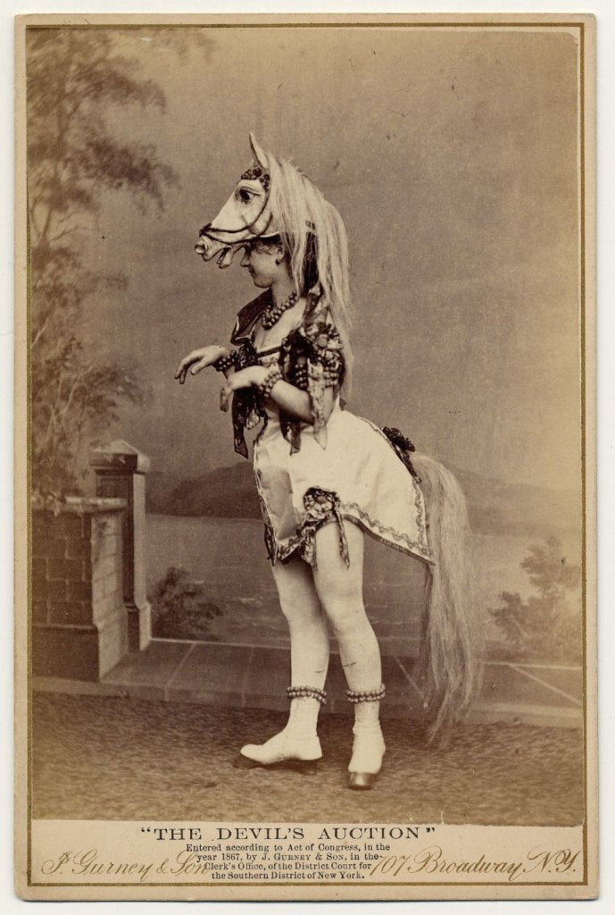 1867. Eliza Blasina wearing horse-head headdress, short costume with attached horsetail, rows of round beads or bells around ankles, wrists, neck and upper arm.
