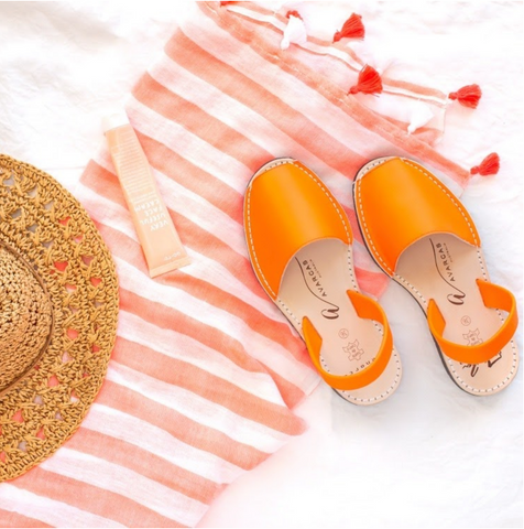 Neon orange avarcas lying on an orange and white striped towel with straw hat