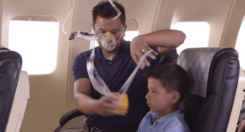 Man helping child put on oxygen mask in airplane