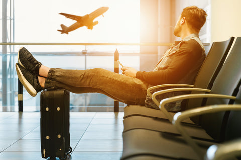 Man Sitting in Airport with Feet on Luggage During Morning