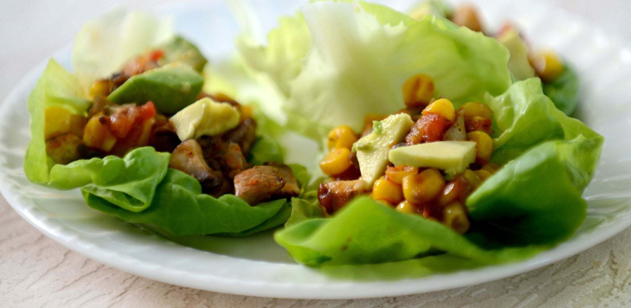 Roasted mushrooms, avocado dices and corn on a lettuce taco shell, on a white plate