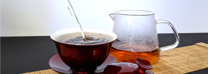 water pours into a gaiwan with brewed black tea in the backgound; the first infusion contains the most caffeine