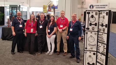 The Stone Harbor team stands in their booth at IBS2023, with a bath hardware display in the foreground.