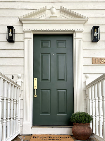A Satin  Brass Munich Handleset on a deep green front door of a white house.