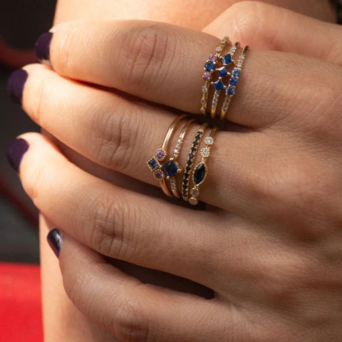 3 Sapphire Equilibrium Gold Ring on model's hand, stacked with other gold rings with colored gemstones