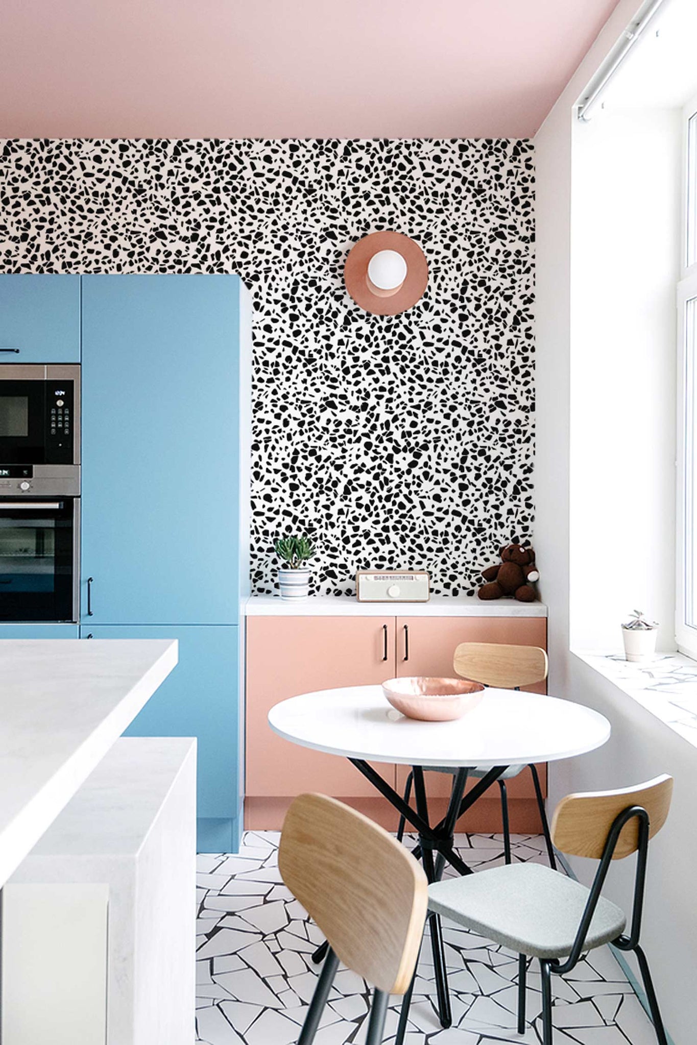 eclectic summer fashion trends of 2022 styled in home interior, eclectic kitchen interior with blue cupboards and black terrazzo floor, pink walls and black terrazzo design removable wallpaper by livettes wallpaper