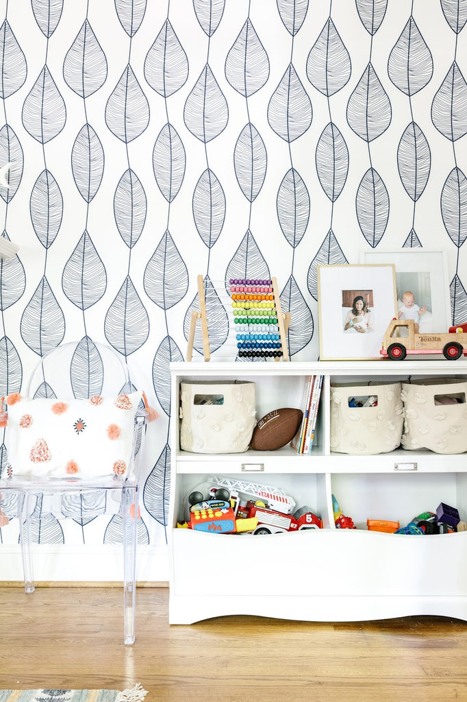 Stripy leaf wallpaper in kid's playroom interior with ghost chairs and white toy storage shelves