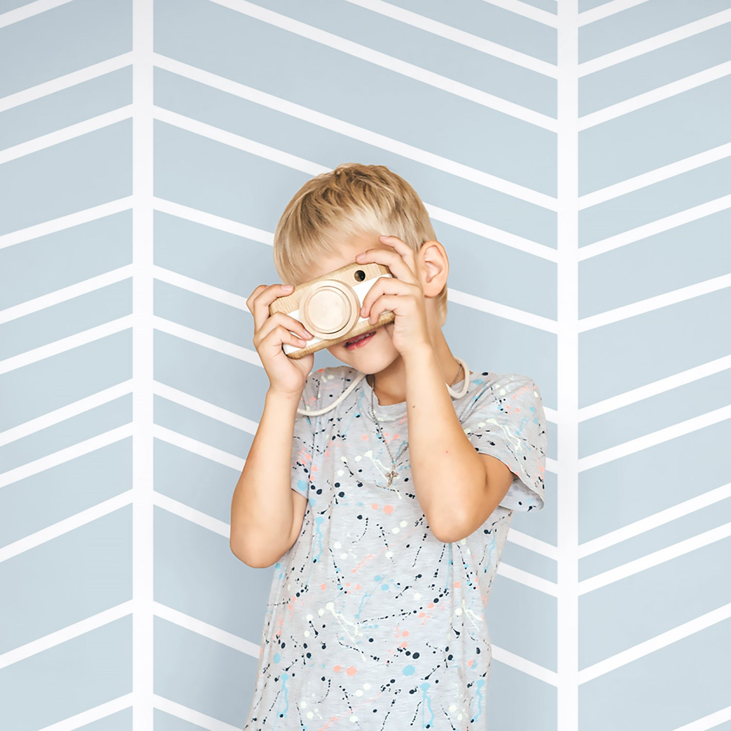 Light blue herringbone wallpaper and boy with toy camera