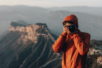 Hiker atop mountain taking picture with mirrorless camera