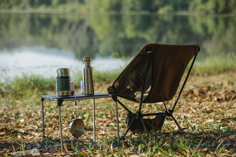 camping chair next to a table with a water bottle by the river shore