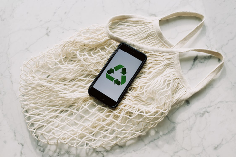 Mobile phone with green recycling sign and mesh bag.