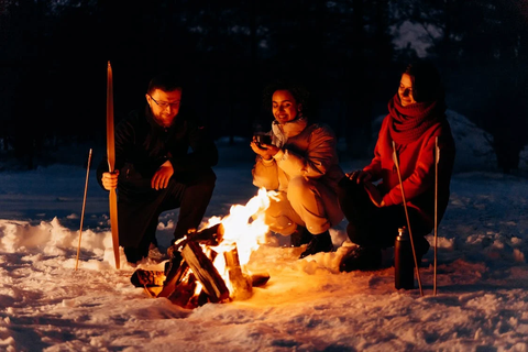 Campers sitting around the fire at a night-time winter trip