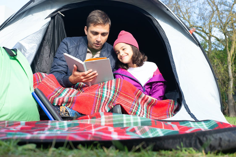 A parent and child reading a book inside a tent