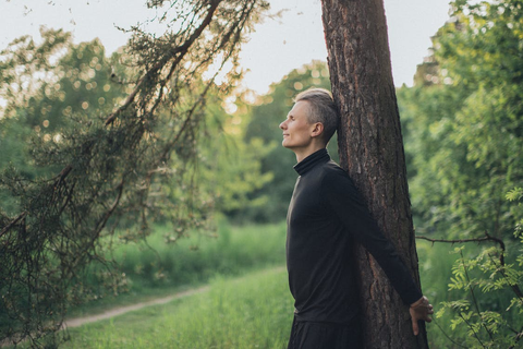 A young man standing near a tree trunk in a forest