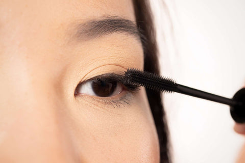 Close up vegan mascara wand applying to outer lashes on Asian model for French look makeup