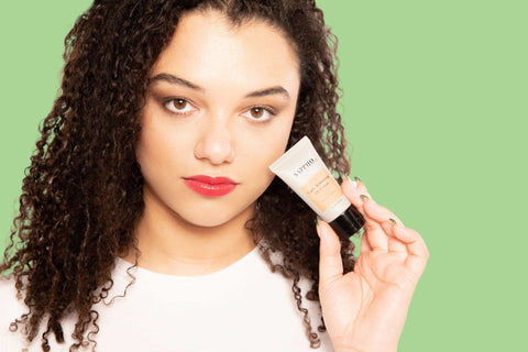 Model holding a CC cream tube close to her face, wearing a natural makeup look